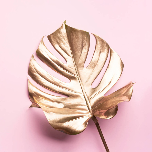 Exotic summer trend in minimal style. Golden tropical palm monstera leaf on pastel pink color background. Shiny and sparkle design, fashion concept. - Fotoğraf, Görsel