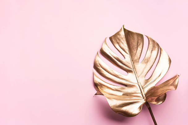 Golden tropical monstera leaf on pink background with copy space. Top view. Flat lay. Creative layout. Exotic summer concept in minimal style - Foto, Bild