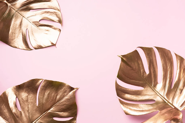 Golden tropical monstera leaf on pink background with copy space. Top view. Flat lay. Creative layout. Exotic summer concept in minimal style - 写真・画像