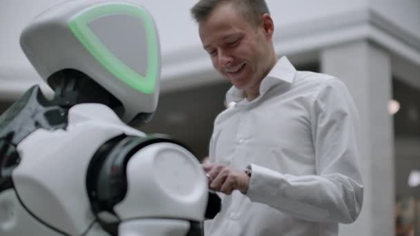 Un uomo in camicia comunica con un robot bianco facendo domande e premendo lo schermo con le dita
. - Filmati, video
