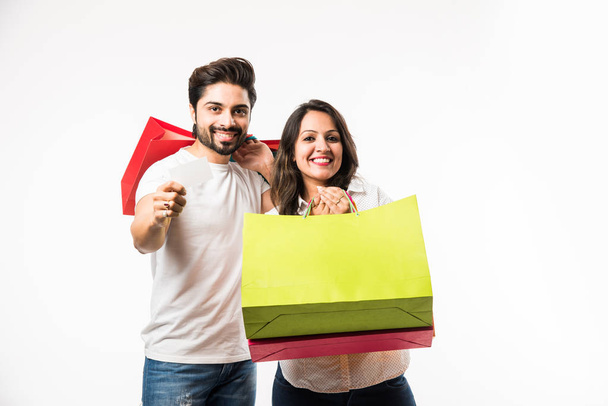 Indian young couple shopping bags and blank debit/credit or electronic card for payment, standing isolated over white background. selective focus - Photo, Image
