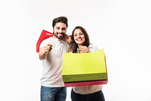 Indian young couple shopping bags and blank debit/credit or electronic card for payment, standing isolated over white background. selective focus - Foto, Imagem