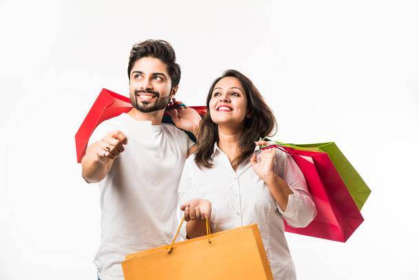 India joven pareja bolsas de compras y en blanco débito / crédito o tarjeta electrónica para el pago, de pie aislado sobre fondo blanco. enfoque selectivo
 - Foto, imagen