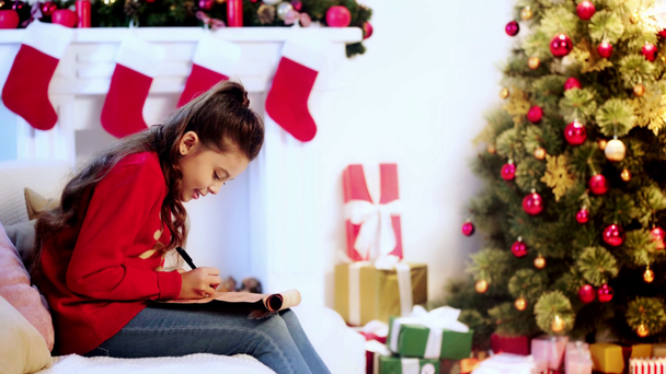 kid writing letter to santa near christmas tree - Кадри, відео