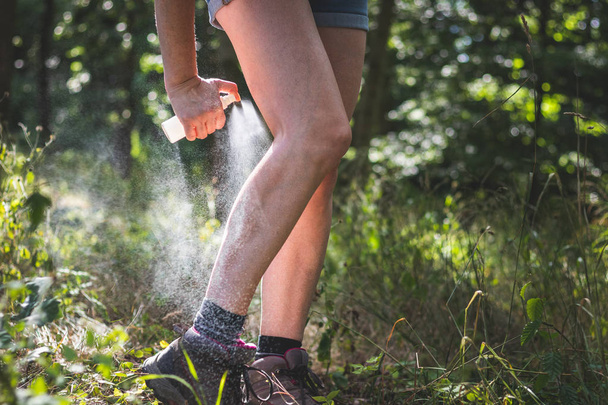 Repelente de insectos. Mujer aplicando repelente de mosquitos en sus piernas en el bosque. Protección de la piel contra las garrapatas y otros insectos
.  - Foto, imagen