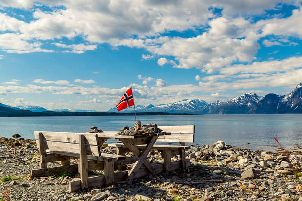 Picnic site rest stop area wooden table decoration and norwegian flag on lake fjord shore. Holidays relaxation on trip. Scandinavia Europe. - Photo, Image