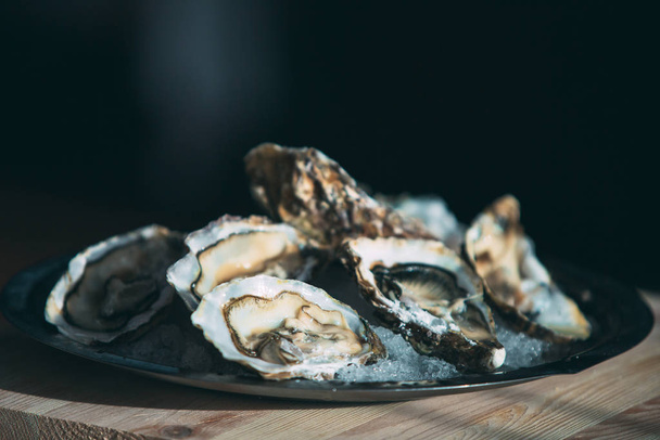 Oysters on the black plate on wooden background. - Valokuva, kuva