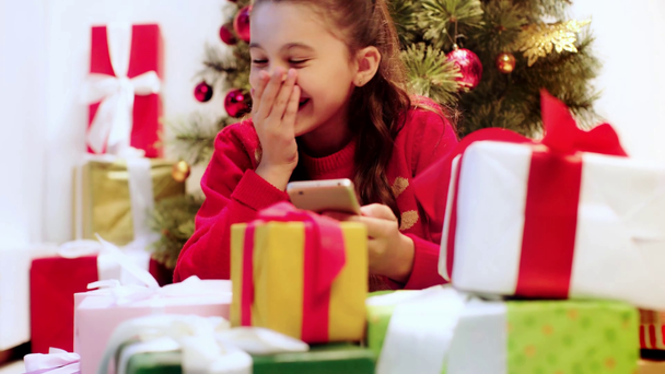 Kind nutzt Smartphone in der Nähe von Geschenken und Eltern - Filmmaterial, Video
