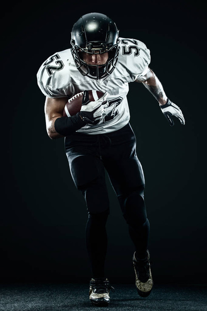 American football sportsman player in helmet isolated run in action on black background. Sport and motivation wallpaper. - Foto, Imagem