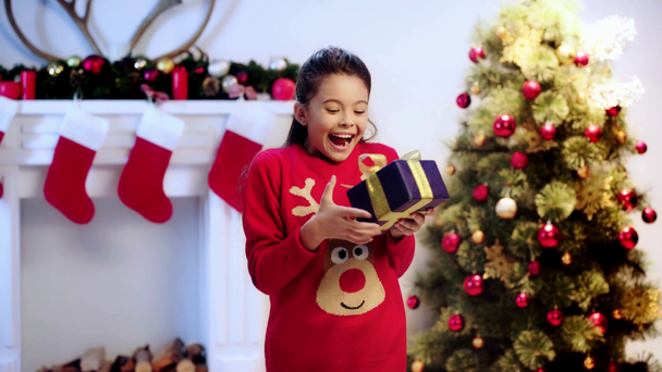 glückliches Kind hält Geschenk und gestikuliert an Weihnachten  - Filmmaterial, Video