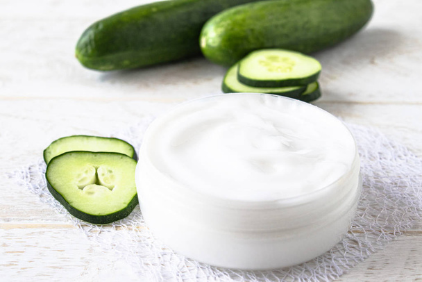 Face cream in a white jar with slices of fresh cucumbers on a white wooden background. - Zdjęcie, obraz