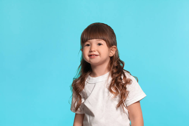 Beautiful little girl wearing in a white t-shirt is posing against a blue studio background. - Photo, Image