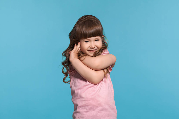 Όμορφο κοριτσάκι φορώντας ένα ροζ μπλουζάκι ποζάρει σε ένα μπλε φόντο στούντιο. - Φωτογραφία, εικόνα