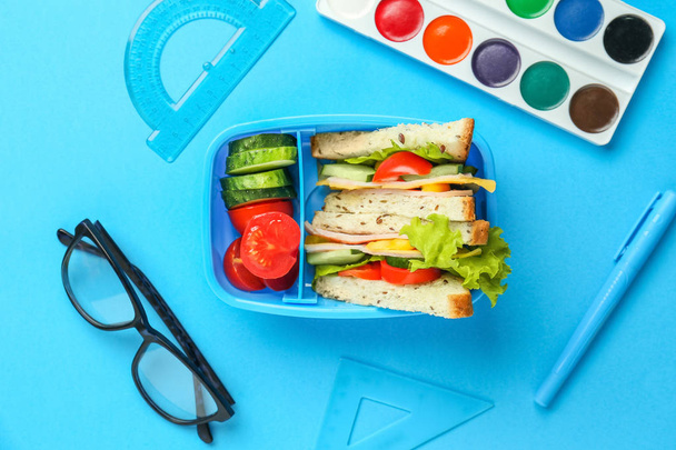 School lunch box with tasty food and stationery on color background - Photo, Image