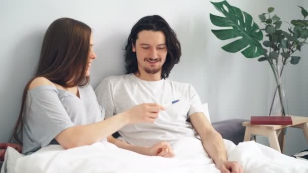 Pregnant girl giving guy pregnancy test, couple kissing hugging in bed at home - Filmagem, Vídeo
