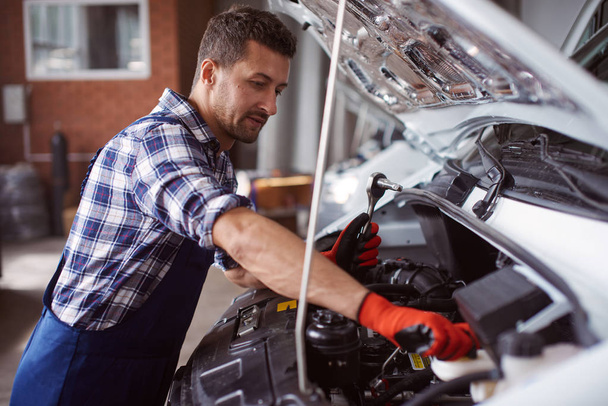 Man works at the car service under the fixation of a broken car engine. - Foto, afbeelding