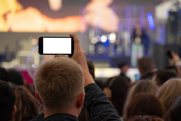 Un homme tient un smartphone dans ses mains et enregistre ou diffuse en direct un concert de rue parmi une foule de fans. Vue de l'arrière. Un blanc pour intégrer n'importe quelle image au lieu d'un écran blanc
. - Photo, image