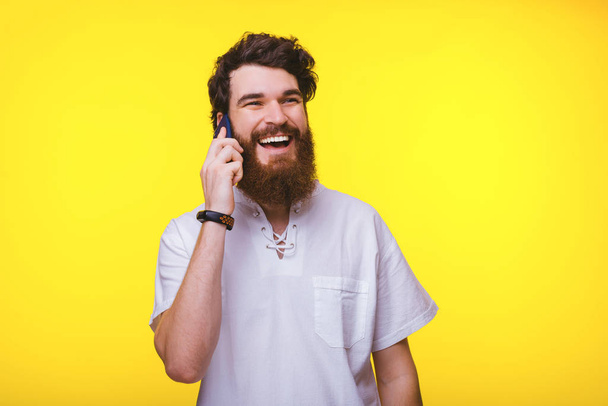 Photo of young smiling man talking on smartphone over yellow background - Photo, Image