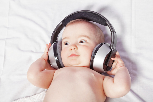 Baby girl lying down listening to music with wireless headphones - Foto, Imagem
