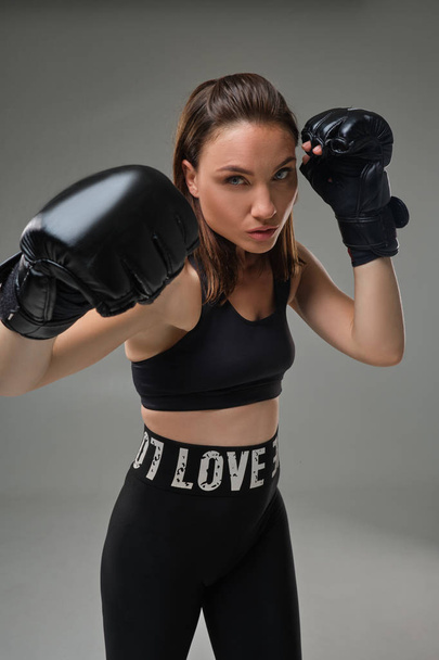 Athletic woman in boxing gloves is practicing karate in studio. - Фото, изображение