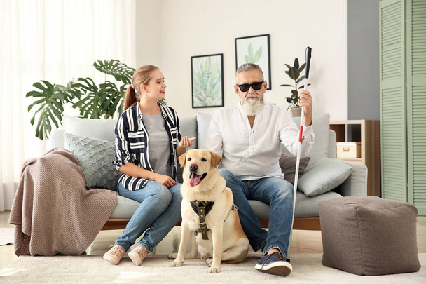 Сліпий зрілий чоловік з дочкою і собакою-поводирем вдома
 - Фото, зображення