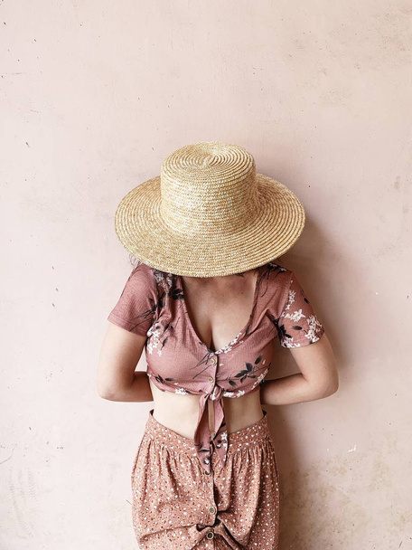 Concetto femminile di moda. Giovane donna in gonna rosa, camicetta rosa corta e cappello di paglia in piedi vicino al muro rosa. Blog di bellezza
. - Foto, immagini