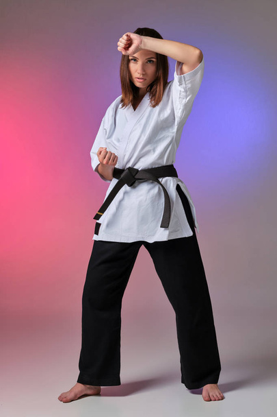 Urheilullinen nainen perinteisessä kimonossa harjoittelee karatea studiossa
. - Valokuva, kuva