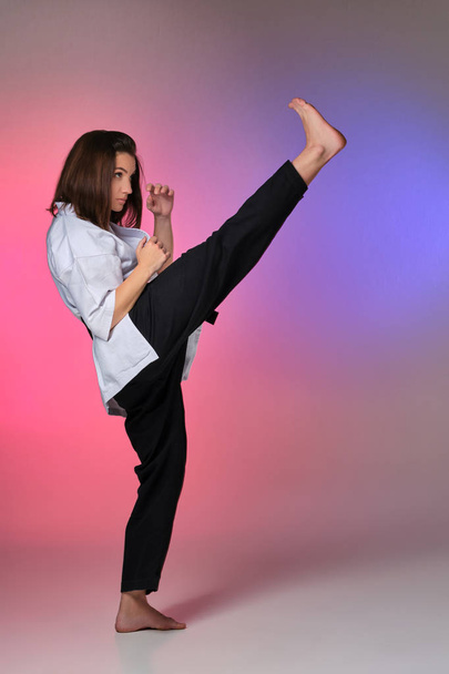 Athletic woman in traditional kimono is practicing karate in studio. - Photo, Image