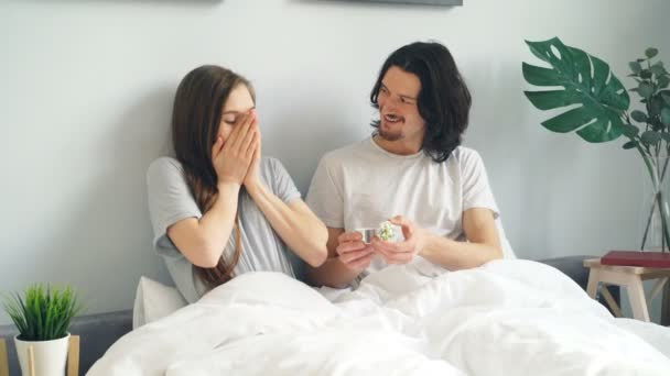 Young man making marriage proposal to girl putting ring on finger in bed at home - Πλάνα, βίντεο