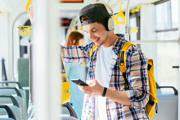 Молодой человек стоит в автобусе с наушниками на голове и слушает музыку
. - Фото, изображение