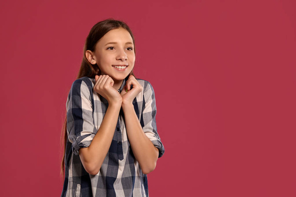 Gyönyörű tizenéves lány egy alkalmi kockás póló pózol ellen rózsaszín stúdió háttérben. - Fotó, kép