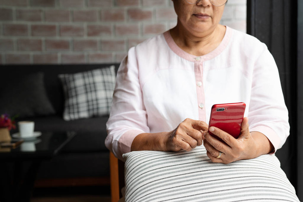 anziana donna utilizzando il telefono cellulare mentre seduto sul divano a casa - Foto, immagini