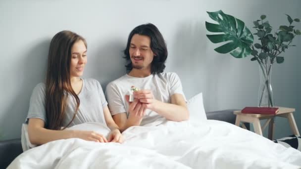 Loving guy making proposal to girlfriend in bed kissing giving ring in box - Кадры, видео