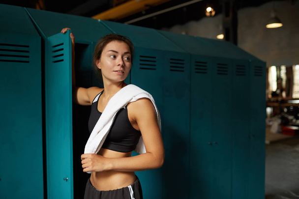 Portrait à la taille dramatique d'une jeune femme debout près d'un casier dans un club de sport et regardant ailleurs, copiant l'espace
 - Photo, image