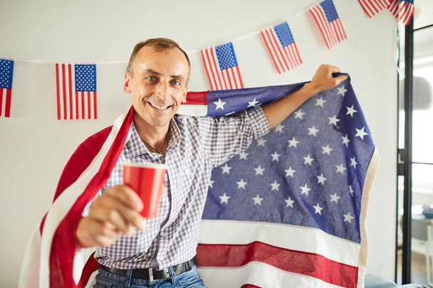 Πορτρέτο του ευτυχισμένο ώριμο άνδρα κουνώντας την αμερικανική σημαία και χαμογελαστά ευτυχισμένα στη φωτογραφική μηχανή, αντίγραφο χώρου - Φωτογραφία, εικόνα