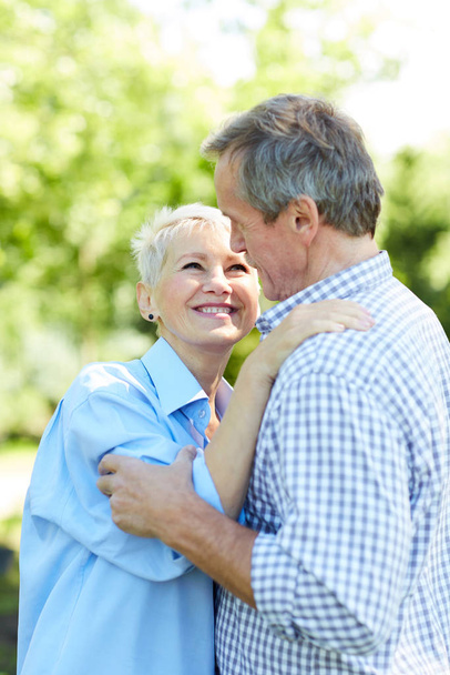 Taille up portret van gelukkige Senior paar kijkend naar elkaar terwijl omarmen in zomerpark - Foto, afbeelding