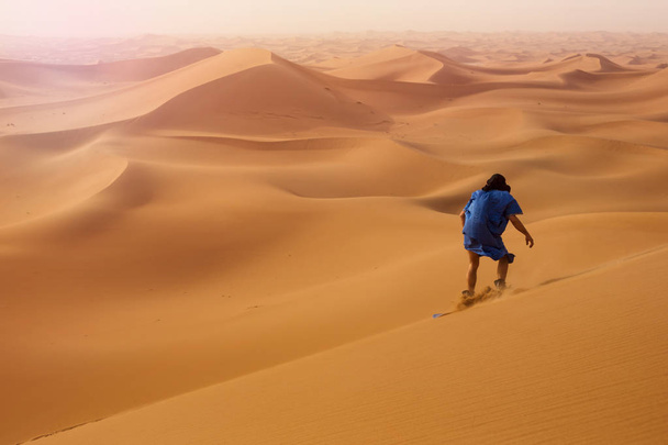 vue arrière du sandboarder habillé en Touareg Gandoura chevauchant le sable sur les dunes d'Erg Cheggaga au Maroc
  - Photo, image