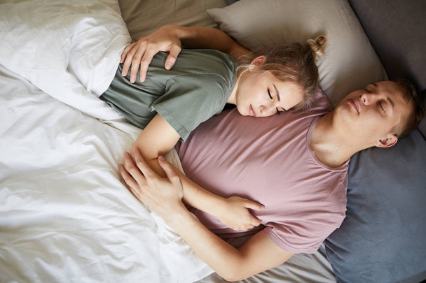 Geceleri battaniye altında birbirlerine yakın uyuyan tişörtlü barışçıl genç eşler - Fotoğraf, Görsel