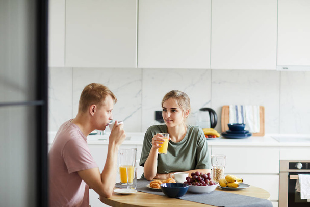 Young woman and her husband drinking orange juice by breakfast in the morning - Photo, Image