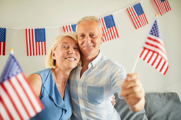 Portrait of happy senior couple waving American flag and smiling at camera - 写真・画像