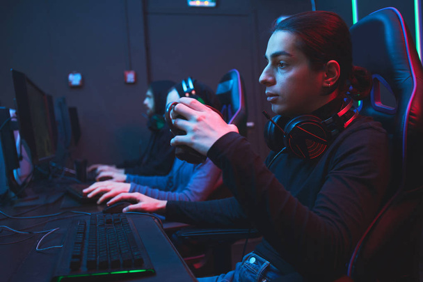 Pensive fiatal programozó fekete nyakú ül az asztalnál, és ivott kávét bögre munka közben a szoftver sötét szobában - Fotó, kép
