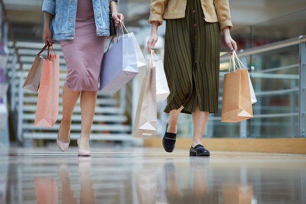 Nerozeznatelné ženy ve stylových oblecích, které se spojily nad nákupním střediskem a přepravují nákupní tašky - Fotografie, Obrázek