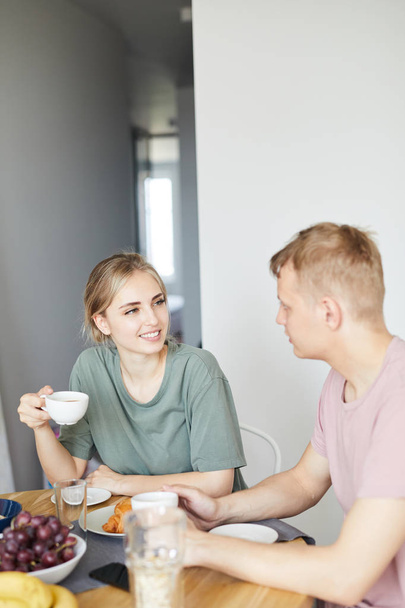 朝の朝食でお茶を飲みながら夫に話しかける可愛い若い女性 - 写真・画像