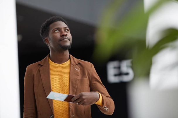 Content handsome black man with beard wearing brown jacket checking flight number while looking at departure board - Photo, Image