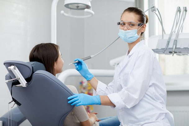 Portret van lachende vrouwelijke tandarts kijkend naar camera tijdens het werken met kind patiënt, kopieer ruimte - Foto, afbeelding