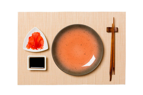 Üres kerek barna lemez pálcika a sushi, gyömbér és szójaszósz a barna sushi szőnyeg háttérben. Felülnézet másolási területtel a tervezéshez - Fotó, kép
