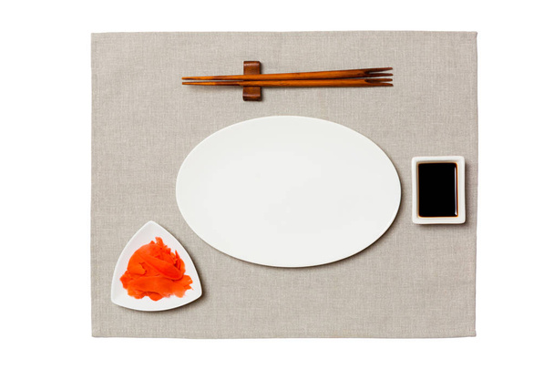 Prázdná oválná bílá deska s hůlky pro sushi, zázvorové a sójové omáčky na šedém ubrousku. Pohled shora s místem kopírování pro návrh - Fotografie, Obrázek