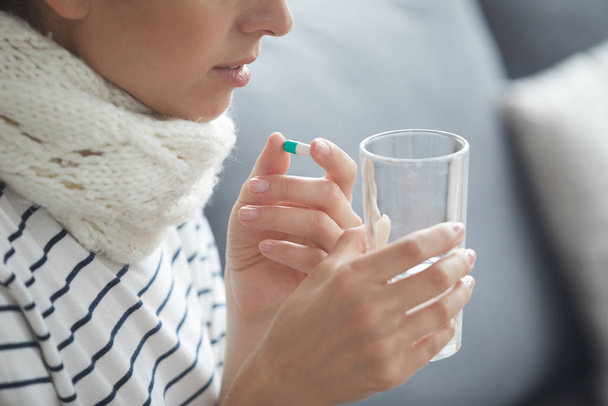 Close-up of sick young woman in scarf drinking water with pills while treating inflamed throat - Photo, Image