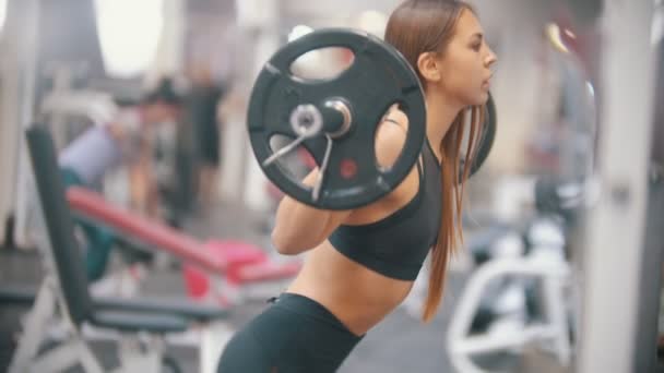 Una atleta entrenando en el gimnasio, sentada con una mancuerna en los hombros
 - Metraje, vídeo