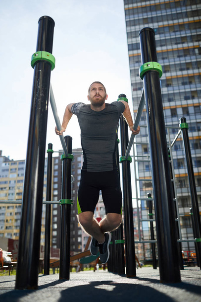 Визначений молодий бородатий чоловік у спортивному одязі використовує відкриті тяги для тренувань біля будинку
 - Фото, зображення